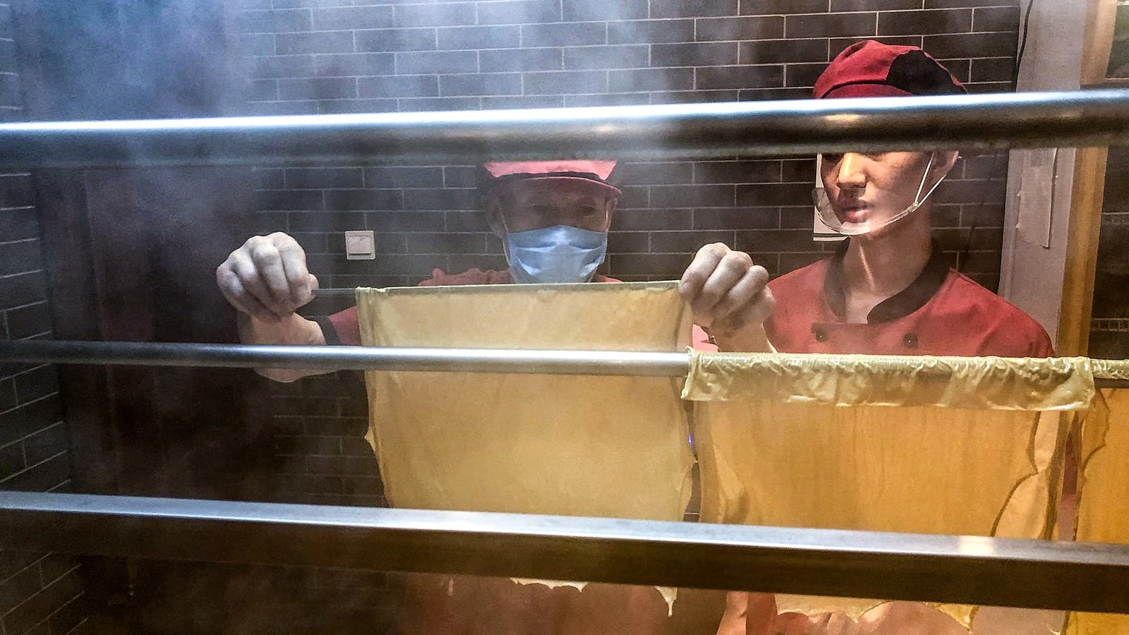 Workers lifting tofu skin sheets used to compare a flatter soy-based texture route