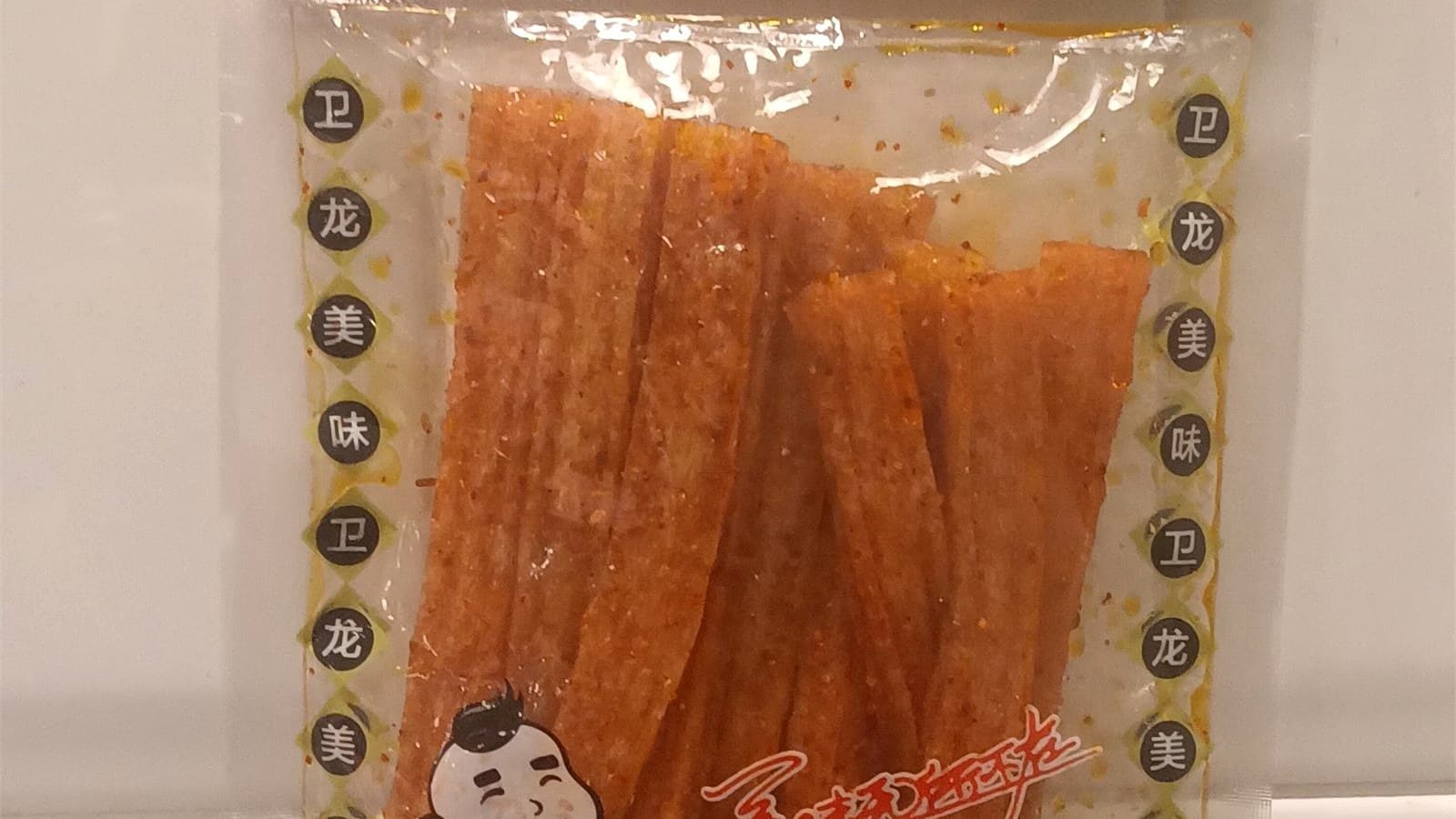 A sealed Weilong spicy gluten package standing beside the opened product strips
